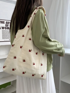 Model wearing a cream canvas tote bag with embroidered cherry patterns in a cozy room