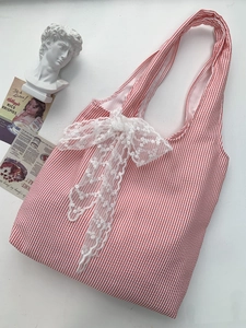 Detail of red and white striped tote bag featuring a large decorative white lace bow