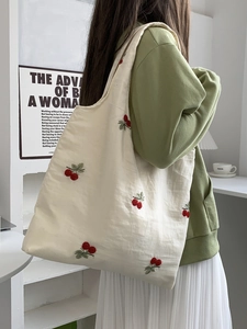 Close-up of cream canvas tote bag featuring delicate red cherry embroidery details
