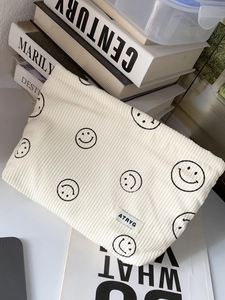 Beige corduroy makeup bag with black smiley faces and zipper closure on vintage books