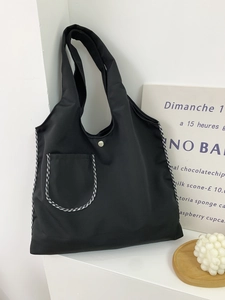 Detail of black nylon tote bag with checkerboard piping and silver snap button closure