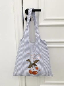 Minimalist blue striped canvas tote bag with cherry print hanging on a door handle