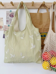 Detail of light green canvas tote bag with white floral embroidery hanging on wooden hook