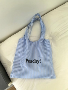 Close-up of blue and white striped tote bag featuring Peachy lettering on soft canvas fabric