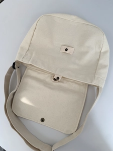 Detail showing the heavy textured canvas material and metal snap button of the beige bag
