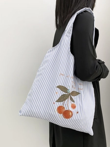 Detail view of a blue striped canvas tote bag with cherry print worn by a model