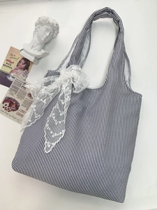 Detail view of blue striped canvas tote bag featuring delicate white lace floral bow