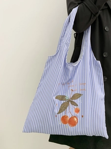 Detail of blue striped canvas tote bag featuring a red cherry print and soft fabric texture