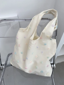 Detailed embroidery of colorful flowers on a cream canvas tote bag over a chair