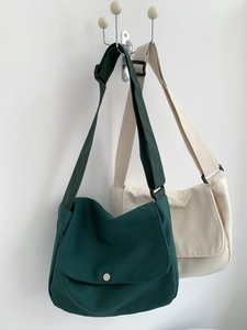 Detail of minimalist canvas crossbody bags in dark green and beige hanging on a wall