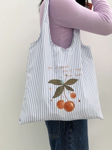 Detail of striped canvas tote bag with cherry print and orange text on model shoulder