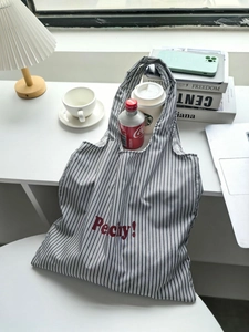 Detail of striped nylon tote bag with Peachy! print used as a laptop and coffee carrier