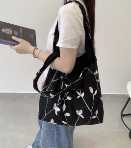 Macro detail of black canvas tote bag featuring intricate white leaf embroidery patterns