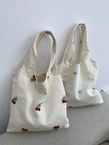 Close-up of floral cherry and bow embroidery details on beige canvas tote bags