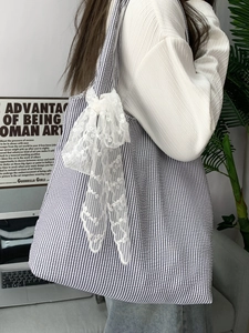 Detail of grey striped canvas tote bag featuring a large white lace bow accessory