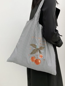 Close-up of a gray striped canvas shoulder bag with cherry print on a model