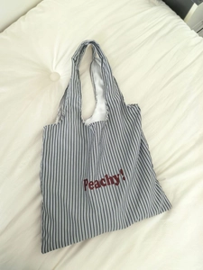 Detail of striped nylon tote bag with red Peachy text on a white textured background