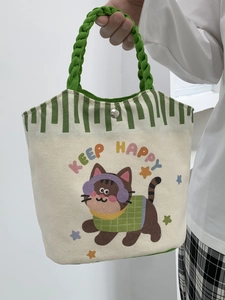 Detail of canvas tote bag with cartoon cat illustration and green braided handle