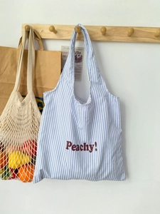 Close-up of blue and white striped canvas tote bag with Peachy text on a wooden wall hook
