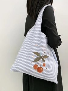Detail of blue striped canvas tote bag featuring red cherry print and shoulder strap
