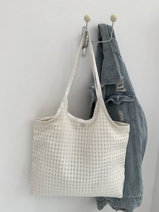 Minimalist beige checkered canvas tote bag hanging next to a blue denim jacket