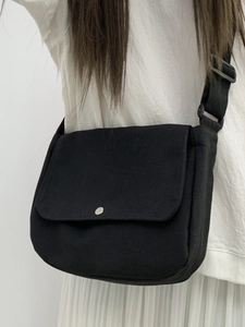 Close-up of black canvas messenger bag with silver snap button and adjustable shoulder strap