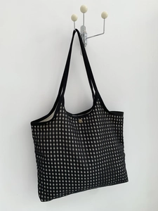 Close-up of black and white checkered canvas tote bag with gold metal snap button closure