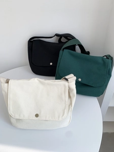 Close-up of canvas crossbody bags in off-white, green, and black with metal snaps