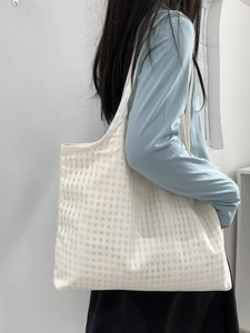 Detail of white checkered canvas tote bag with lightweight textured mesh fabric on shoulder