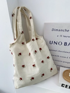 Detailed embroidery of small red flowers on a cream-white canvas tote bag texture
