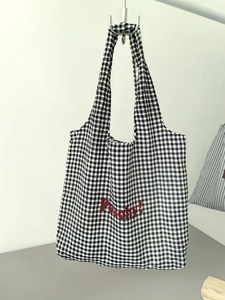 Detail of black and white gingham canvas tote with red Peachy text on metal hanger