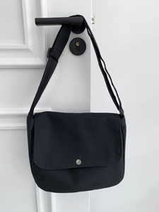 Minimalist black canvas messenger bag with adjustable strap and silver metal button snap
