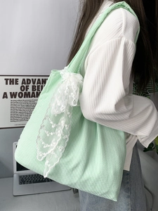 Close-up of green striped canvas tote bag with decorative white lace bow detailing