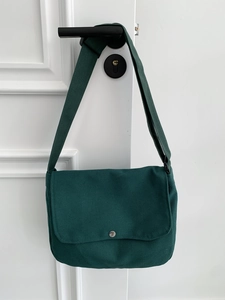 Detail of dark green canvas messenger bag featuring a silver metal snap button and flap