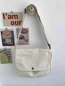 Detail of off-white canvas crossbody bag showing brass snap button and adjustable strap