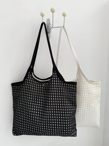 Detail of minimalist checkered mesh tote bags hanging on a modern metal wall hook