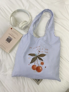 Detail of blue striped canvas tote bag with cherry print and integrated handle design