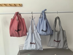 Detail showing four assorted striped and checkered nylon tote bags with Peachy! print
