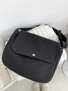 Black canvas messenger bag featuring a large flap and silver metal buckle on a suitcase