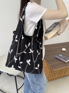 Detailed side view of black canvas tote bag with white leaf embroidery worn by a model