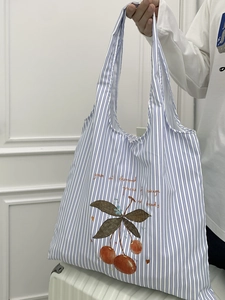 Detail shot of blue striped canvas tote bag featuring a red cherry print and carry handles