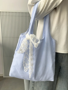 Blue and white seersucker tote bag with white lace bow detail worn by a model