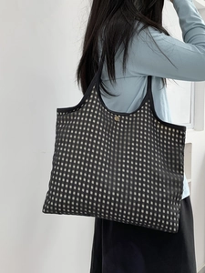 Detail of checkered tote bag showing black shoulder strap and gold metallic buckle closure