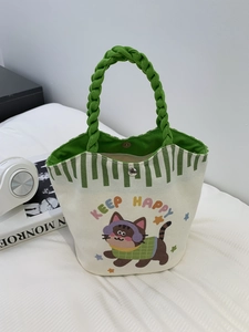 Detail of small canvas tote bag with cartoon cat print and green woven handles