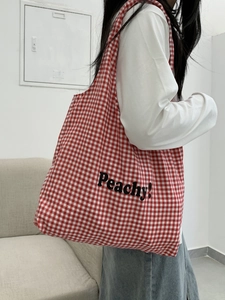 Large red checkered canvas tote bag with Peachy text worn by a model in a home setting