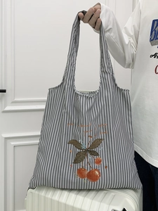 Detail of striped canvas tote bag with cherry graphic placed on a white suitcase