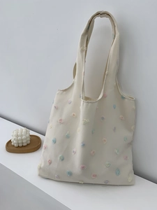 Detail of colorful hand-sewn 3D floral embroidery on a white canvas tote bag