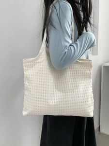 Detail view of the white checkered canvas tote bag worn on shoulder in minimalist interior