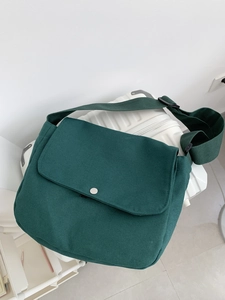 Dark green canvas messenger bag with large flap and metal button on a white suitcase