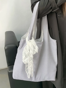 Detail of blue striped canvas tote bag featuring a white lace bow on the shoulder strap